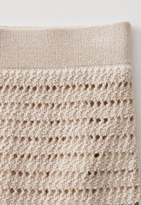 Beige gestrickter Pullover mit einem strukturierten Muster und offenen Löchern, abgeschlossen mit einem gerippten Saum oben für zusätzlichen Stretch und Komfort.
