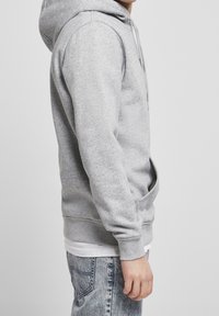 Grijze hoodie gemaakt van fleece, met een kangoeroezak, geribbelde manchetten en zoom, zijaanzicht met lichtblauwe jeans.