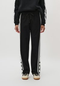 Sorte joggebukser med hvite side-striper, med trykknapper langs sømmen. Laget av mykt stoff med elastisk midje og snøring.
