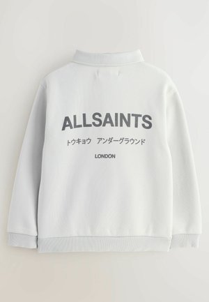 Pelēks džemperis ar polo apkakli, ar lielu melnu "ALLSAINTS" logo un ne-latīņu tekstu aizmugurē, ribotām piedurknēm un apakšmali.