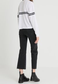 Vit långärmad topp med svarta ränder över ryggen, kombinerad med högmidjade svarta cropped jeans och svarta snörstövlar.