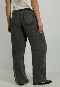 Pantalon en denim gris à jambes larges avec des coutures visibles, deux poches arrière et une taille élastique. La texture semble douce avec une finition délavée.