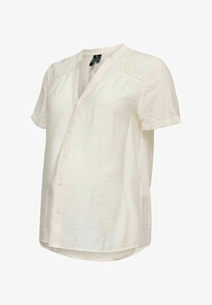 Crèmekleurige blouse met korte mouwen, subtiele bloemenborduursels op de schouders, een knoopsluiting aan de voorkant en een zachte, licht getextureerde stof.