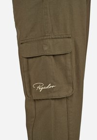 Olive žalia spalvos krovininės kelnės, pagamintos iš minkštos medžiagos, turinčios kišenę su uždengimu ir įsiuvinėtą "Pegador" logotipą šviesiai rudos spalvos.