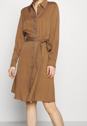 Brązowa sukienka koszulowa z długim rękawem, wzorzysta, z guzikami z przodu i paskiem w talii, noszona przez osobę na jednolitym jasnym tle.