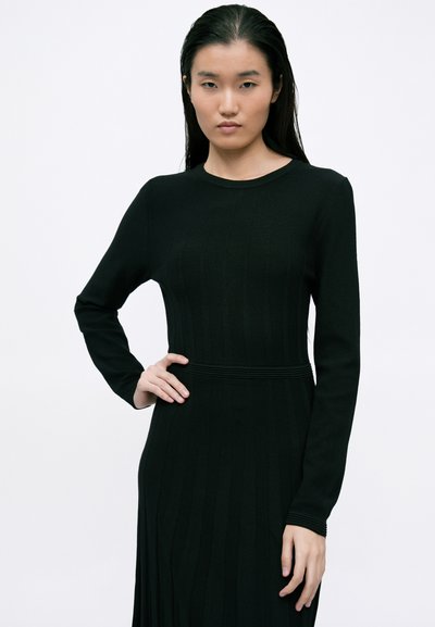 Vestido preto de manga longa com uma textura canelada e cintura ajustada. Apresenta um decote redondo e detalhes de riscas verticais por todo o vestido.