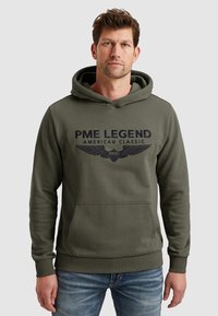 Oliwkowa bluza z kapturem z miękkiego materiału, z przednią kieszenią typu kangur. Posiada haftowane logo "PME LEGEND" oraz design skrzydeł w kolorze granatowym.