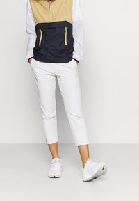 En anoran-färgad halv-zip jacka med en marinblå nederdel, kombinerad med vita cropped byxor och vita sportskor med texturerade sulor.