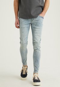 Jeans de mezclilla azul claro con corte ajustado, sutil desgaste y acentos desgatados. Combinados con zapatillas marinas y cordones beiges.
