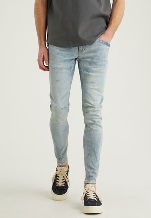 Jeans de mezclilla azul claro con corte ajustado, sutil desgaste y acentos desgatados. Combinados con zapatillas marinas y cordones beiges.