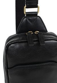 Borsa a tracolla nera in pelle con una superficie liscia, chiusura con zip e accenti in hardware color oro. Presenta una tasca frontale.