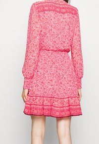 Blommig rosa klänning med långa ärmar, elastisk midja och volangkant. Har intrikata blommönster och en texturerad tyg.