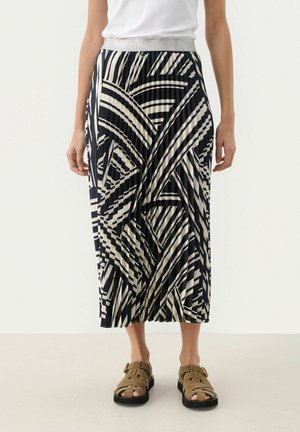 Pleated midi skirt featuring a geometric black and cream pattern, elastic waistband, and a flowy silhouette. Worn with brown strapped sandals.