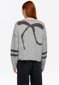Szary sweter z dzianiny o luźnym kroju, z teksturowanym wzorem kokardy na plecach oraz kolorowymi paskami na rękawach.