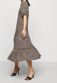 Vestido floral con un cuerpo ajustado, mangas abullonadas y un dobladillo acampanado con volantes. Presenta un patrón multicolor sobre un fondo oscuro. Sandalias de tacón negras.