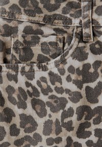 Il tessuto in stampa leopardata presenta un mix di motivi marroni e neri, con una tasca visibile e cuciture beige su materiale denim.