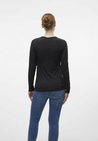 Maglietta nera a maniche lunghe con scollo rotondo, abbinata a jeans blu. Tessuto morbido e design aderente. Stile minimalista.