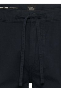 Pantalon bleu marine foncé coupe décontractée avec un cordon de serrage en tissu à la taille et une étiquette de la marque Camel Active sur la ceinture.