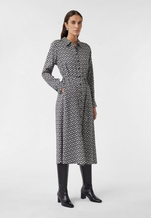 Black and white patterned dress with a collared neckline, button closure, cinched waist, and long sleeves; paired with knee-high black boots.