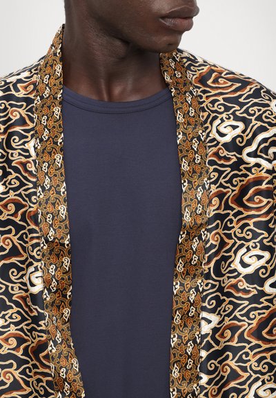 Černý kimono kabát s propracovanými zlatými a hnědými vířivými vzory, s kontrastním zlatě vyšitým lemováním, nošený přes tmavě modrou košili.