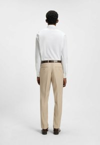 Chemise blanche à manches longues associée à un pantalon habillé beige. La chemise est dotée de boutons aux poignets, et le pantalon a une texture lisse avec des poches arrière.