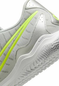 Light gray athletic shoe with a mesh upper, neon yellow accents, textured surface, and a white rubber sole featuring a zigzag tread pattern.