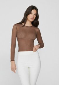 Brauner transparenter Langarm-Oberteil mit Spitzenverzierung, kombiniert mit weißen, enganliegenden Hosen. Glatter Stoff und runder Ausschnitt, minimalistisches Design.