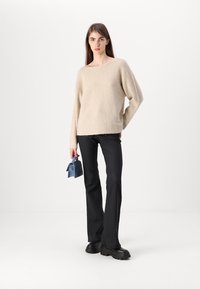 Šviesiai rudas, tekstūruotas megztinis su plačiu apykakle, derinamas su juodais prigludusiais kelnėmis ir mažąja mėlyna rankine. Juodi platforminiai batučiai.