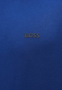 Modré bavlnené tričko s hladkou textúrou a čiernym logom "BOSS" potlačeným na hrudi. Jednoduchý dizajn bez ďalších vzorov.