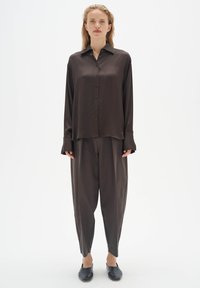 Dark brown satin shirt with a collar, buttons down the front, and long sleeves, paired with loose-fit matching trousers. Black slip-on shoes.