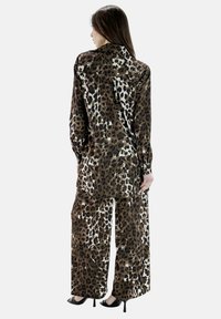 Camicia con stampa leopardata marrone e pantaloni a gamba larga realizzati in tessuto morbido, caratterizzati da una vestibilità comoda e maniche lunghe. Tacchi alti neri completano l'outfit.