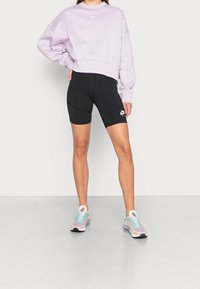Lila kortärmad sweatshirt, svarta cykelshorts med sidopanel, och färgglada sneakers med en gradientdesign och vita accenter.