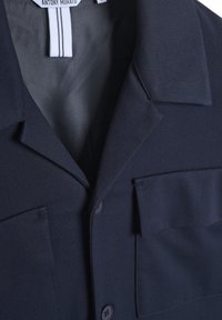 Mornarica blazer s izdvojenim ovratnikom, dva džepa na prsima i glatkom unutrašnjom podstavom. Napravljen od teksturiranog materijala s kopčanjem na dugme.