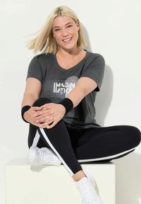 Grijze sport T-shirt met een v-hals en witte grafische print; gecombineerd met zwarte leggings met witte zijkanten en witte sneakers.
