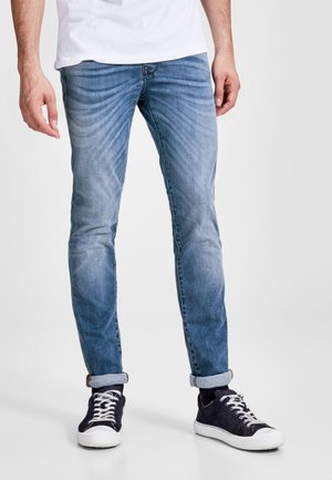 Hellblaue Denim-Jeans mit einem verblassten Design, schmaler Passform und hochgekrempelten Säumen, kombiniert mit dunklen Sneakers mit weißen Akzenten.