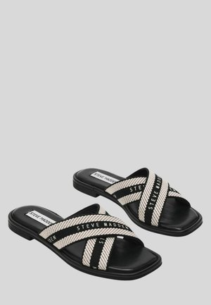 Sandali neri con suola a scivolo e ampie fasce incrociate beige e nere con la scritta "Steve Madden" su uno sfondo grigio.