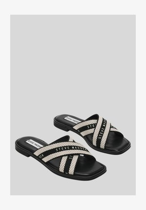Sandali neri con suola a scivolo e ampie fasce incrociate beige e nere con la scritta "Steve Madden" su uno sfondo grigio.