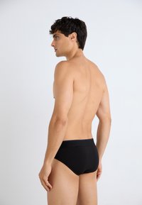 Schwarze Baumwollslips mit glatter Textur, niedrig geschnittenem Design und elastischem Bund, aus seitlicher und hinterer Ansicht gezeigt.
