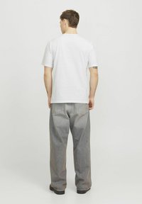 Witte t-shirt met korte mouwen gecombineerd met losse, grijze denim broek met een licht gewassen textuur en achterzakken.