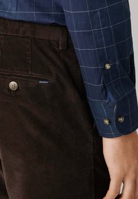 Marineblauw geruit overhemd met knoopmanchetten, in combinatie met bruine ribfluwelen broek met een zijzak en een logopatch.