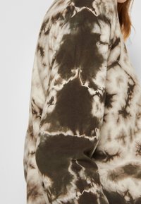 Brązowy i kremowy sweter tie-dye z długimi rękawami, z miękkiego, teksturowanego materiału oraz abstrakcyjnymi wzorami na całej powierzchni.