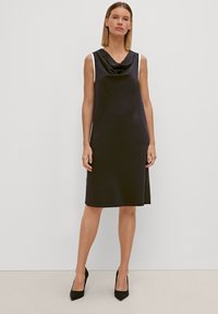 Schwarzes, ärmelloses Kleid mit einem Cowl-Ausschnitt, weißen Akzenten an den Schultern, gerader Silhouette und knielanger Säume.