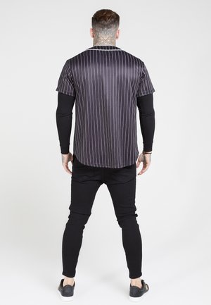 Sort og hvid stribet kortærmet skjorte med satinfinish, buet kant, kombineret med stramme sorte bukser og sorte slip-on sko.