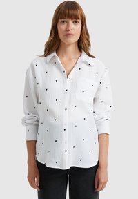 White button-up shirt with black heart patterns, featuring a chest pocket and rolled-up sleeves. Crafted from lightweight, textured fabric.