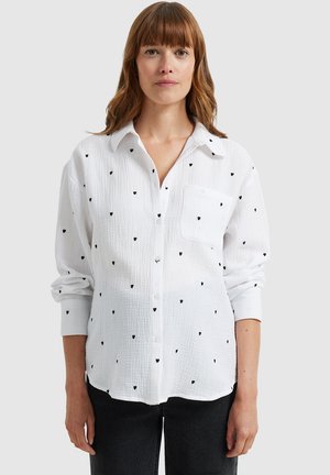 White button-up shirt with black heart patterns, featuring a chest pocket and rolled-up sleeves. Crafted from lightweight, textured fabric.