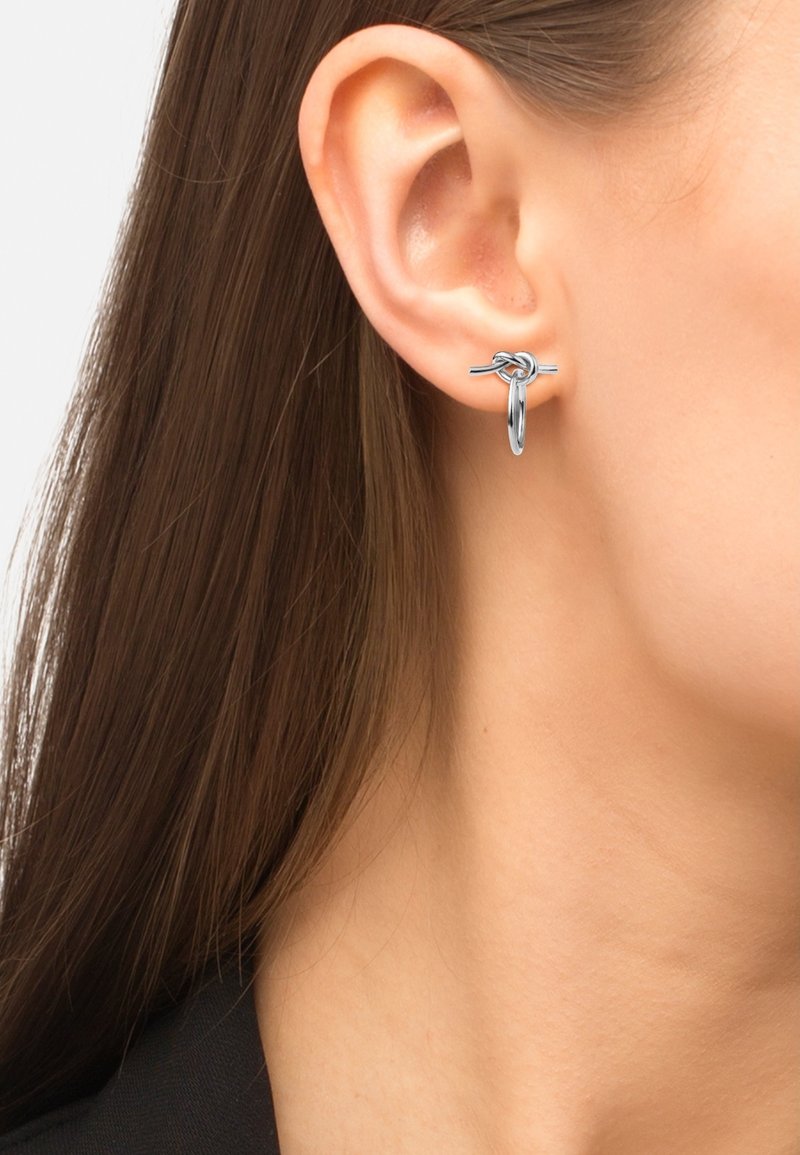 Orecchini a cerchio in argento con design a nodo, finitura lucida, forma rotonda e superficie liscia, indossati all'orecchio di un modello.