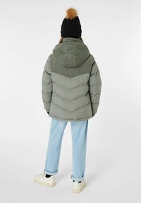Giacca imbottita di colore verde oliva con un design a zigzag, abbinata a jeans azzurri chiari e sneakers bianche. Presenta un cappuccio in corduroy e un cappello lavorato a maglia nero.