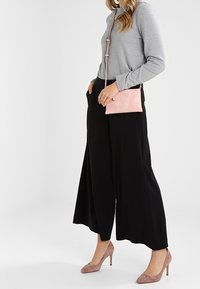 Šedý dlouhý rukáv, černé široké nohavice a světle růžová kabelka. Modelka má na sobě růžové lodičky, se hladkým textilním povrchem.