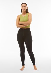 Leggings neri con vita alta e chiusura a zip, abbinati a un crop top verde a coste aderente, tessuto testurizzato e design senza cuciture.