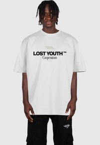 Balta kokvilnas pārspīlētā t-krekla ar melnu un olīvzaļu tekstu "LOST YOUTH™ Cooperations" priekšpusē, īsām piedurknēm un apaļu kakla izgriezumu.